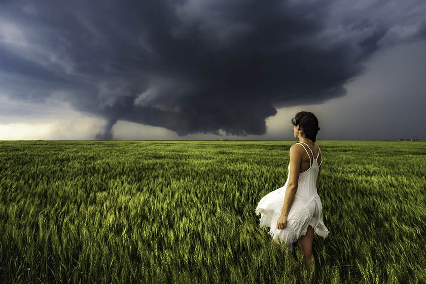 woman standing in wheat field looking at oncoming storm and tornado