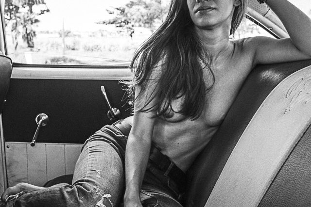 Woman in a car with long hair in jeans and naked from the waist up